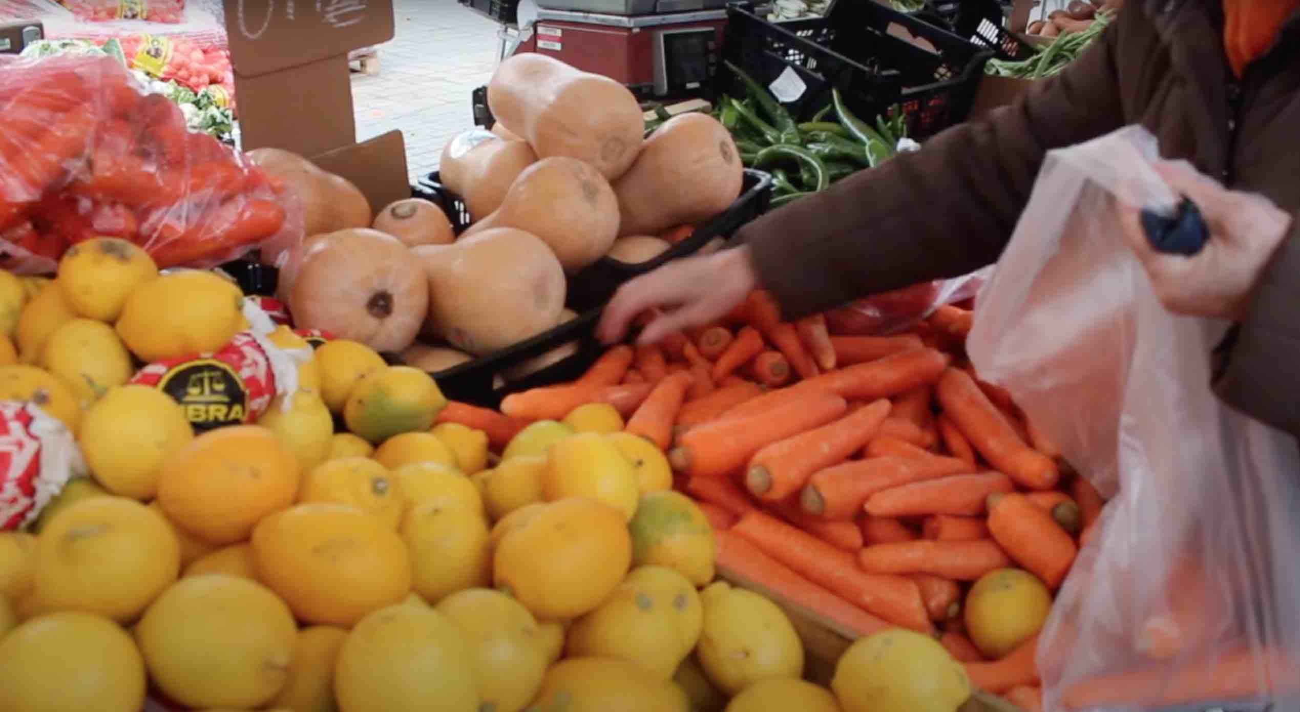 Una señora elige las zanahorias del puesto de fruta en el que está comprando durante el mercadillo de los jueves en La Llagosta